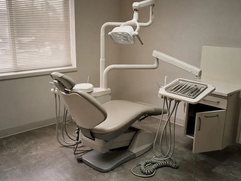 A dental treatment room with a chair and instrument tray in window light.